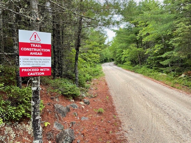 Gravel Trail in the woods with green trees and a red and white sign Trail Construction Ahead