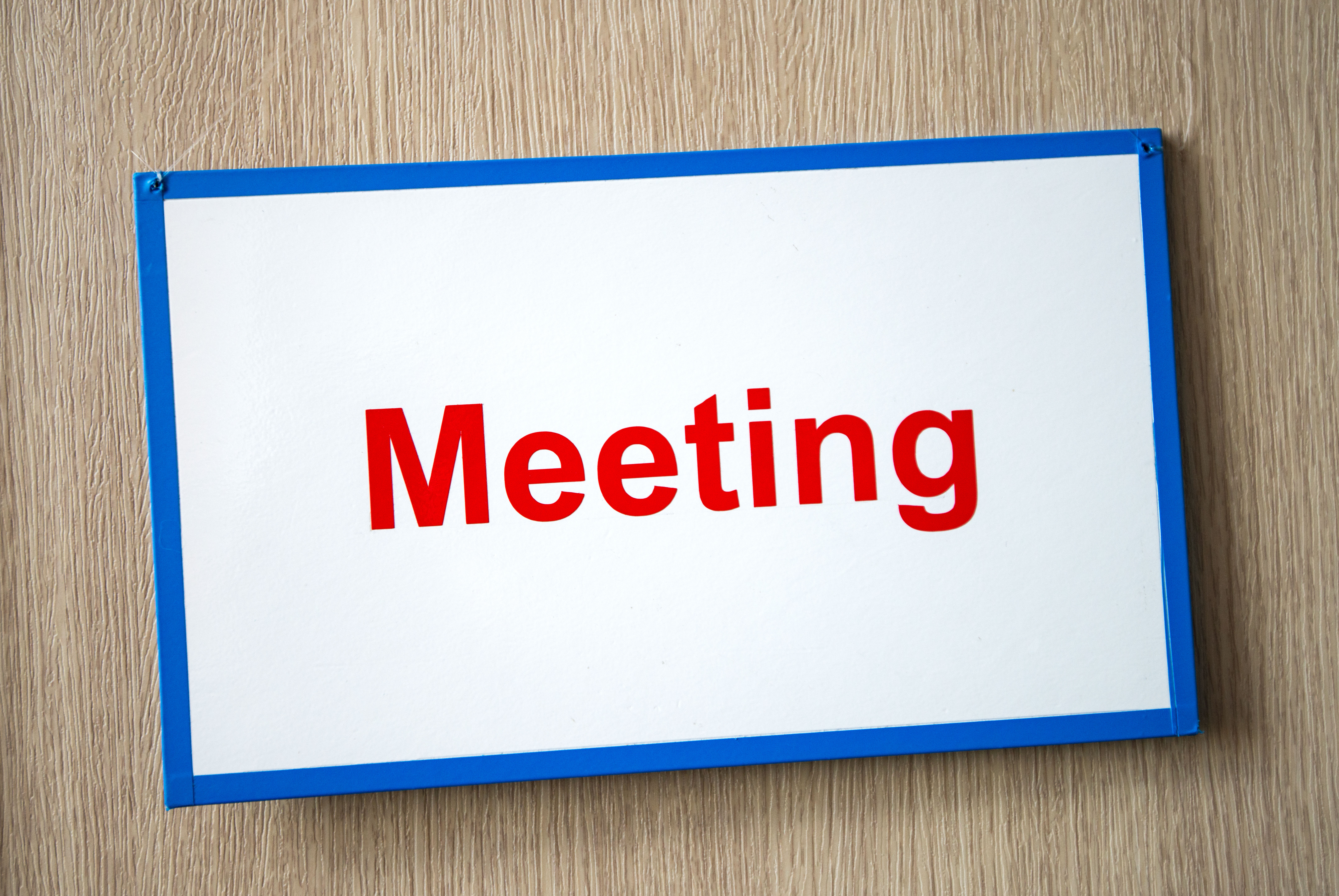 "Meeting" written in red on a sign with a blue border and white background.