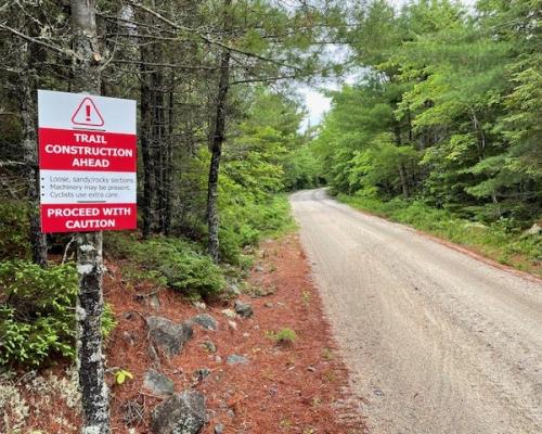 Gravel Trail in the woods with green trees and a red and white sign Trail Construction Ahead