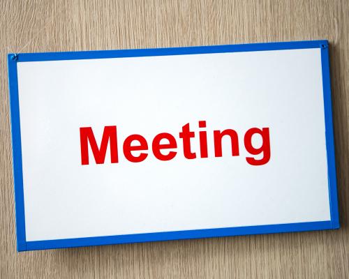 "Meeting" written in red on a sign with a blue border and white background.