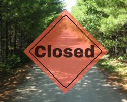 orange closed sign overlaying a forested trail